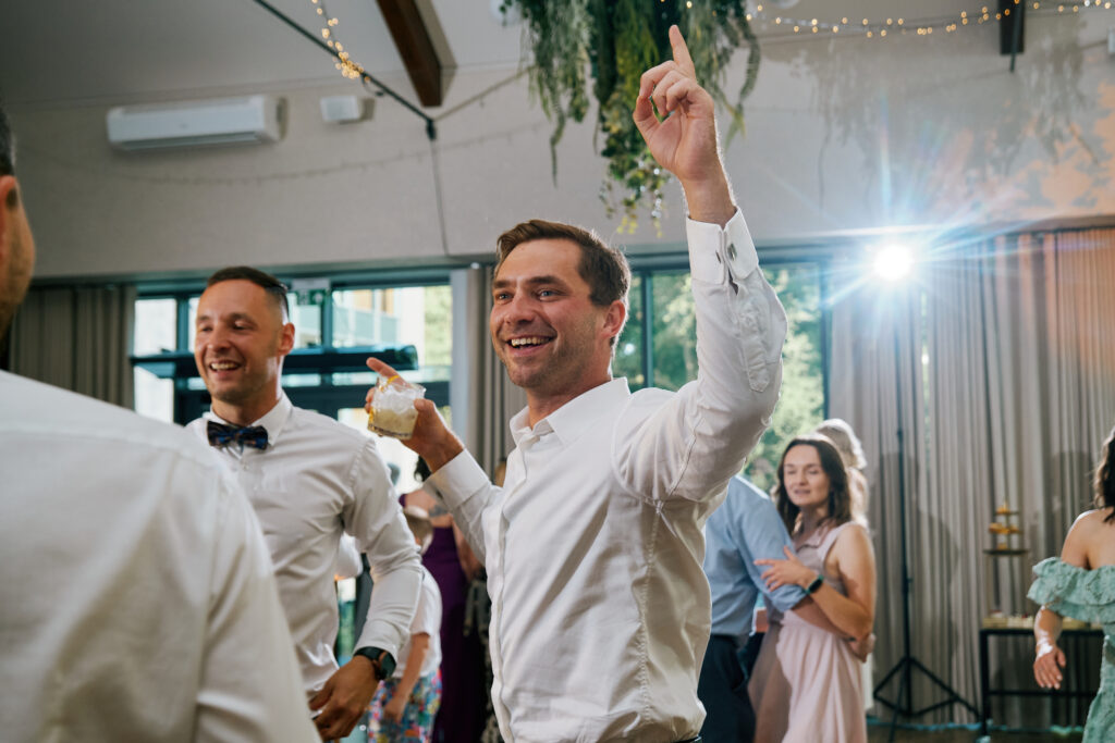 Barman serwuje drinka, ludzie tańczą na przyjęciu, radosna atmosfera w eleganckim wnętrzu.