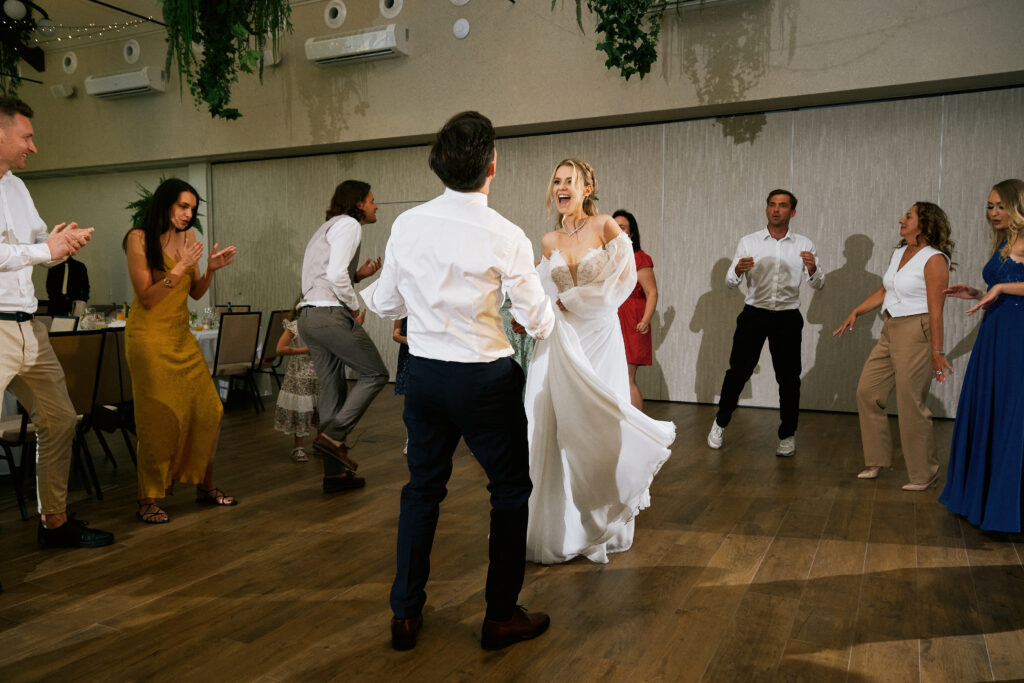 Alt: Para młoda tańczy na weselu w klimatycznym wnętrzu, radosne chwile z gośćmi.