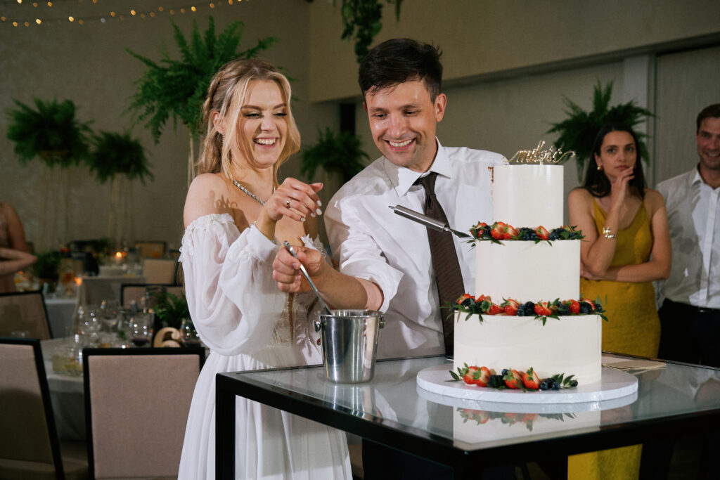 Para młoda kroi tort weselny, nowoczesne zdjęcie obsługi weselnej, profesjonalna fotografia ślubna.