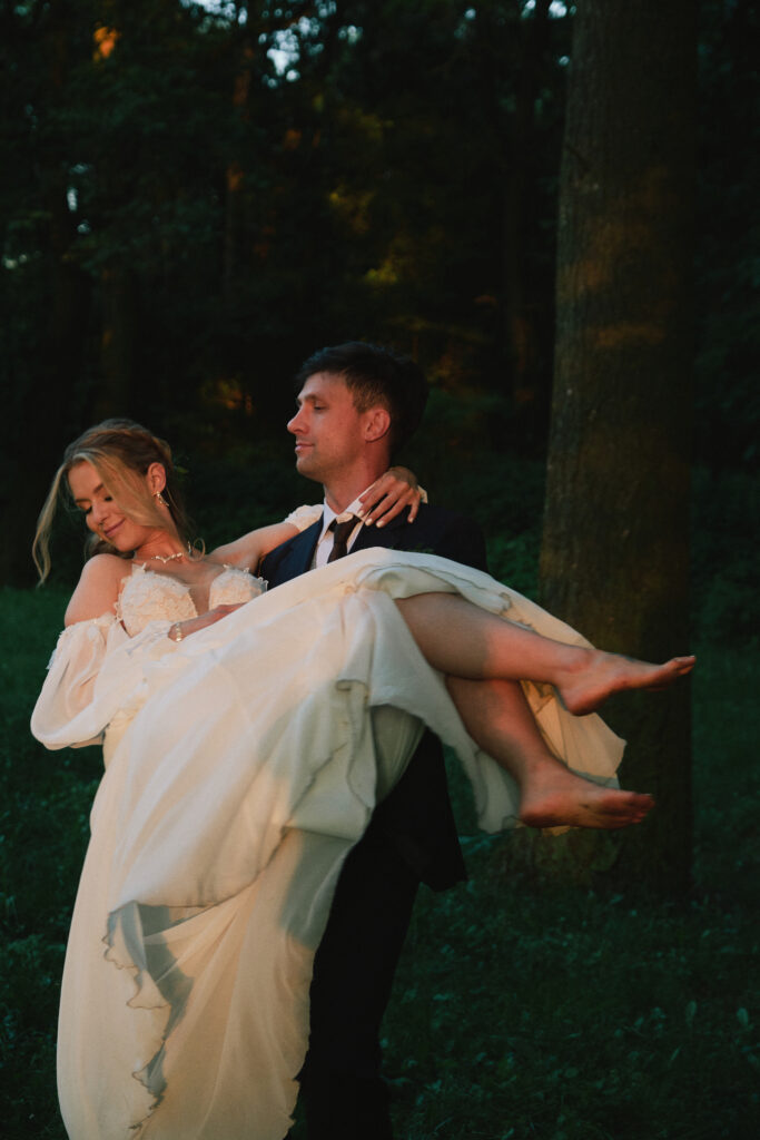 Zdjęcie pary młodej w lesie, mężczyzna niosący kobietę w romantycznej sesji ślubnej.