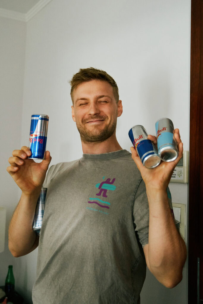 Chłopak trzyma puszki Red Bull, uśmiecha się radośnie, atmosfera w domu, młodość i energia.