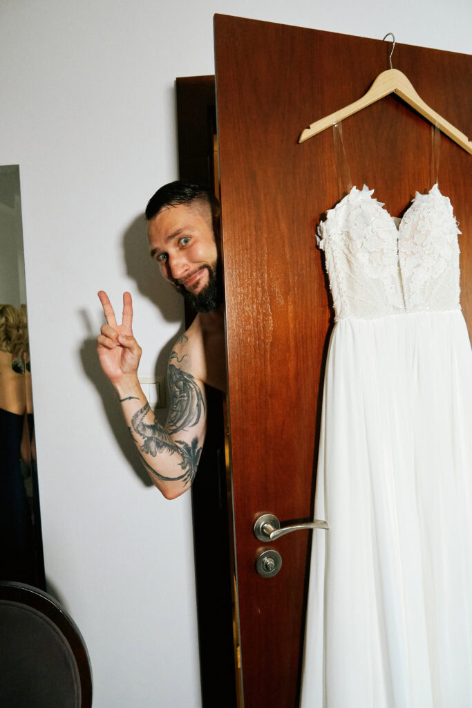 Tatuaż mężczyzny, za nim widoczna suknia ślubna na drążku, w studio ślubnym.