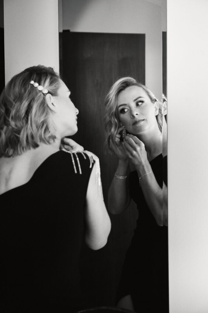 Kobieta zakładająca biżuterię, elegancki look, makijaż, przygotowania do wieczoru.