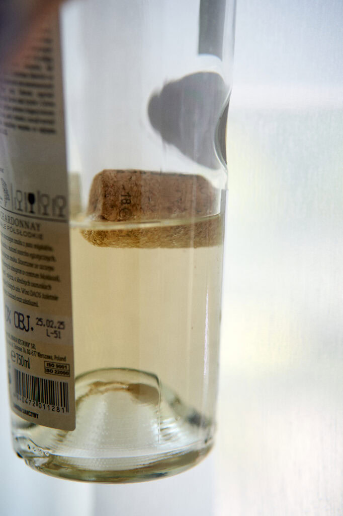 Szklanka białego wina z korkiem, eleganckie ustawienie na tle białej ściany.