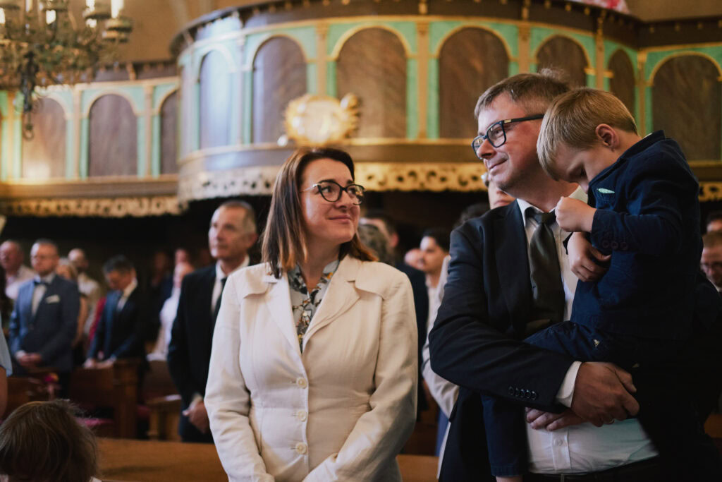 Fotografia z uroczystości religijnej, rodzinna atmosfera, uczestnicy w eleganckich strojach.