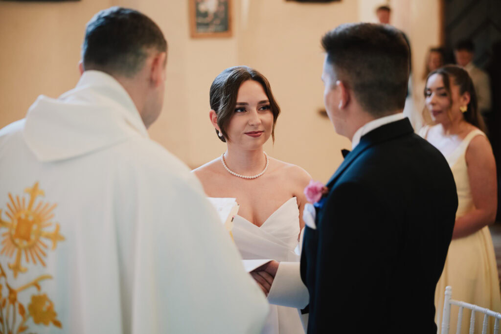 Przyjęcie ślubne z parą młodą i księdzem podczas uroczystości w kościele.