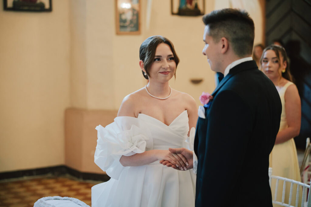 Alt="Panna młoda i pan młody podczas uroczystości ślubnej, romantyczny moment w eleganckim wnętrzu".