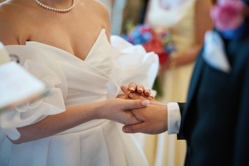 Delikatne zbliżenie na dłonie młodej pary podczas ślubu, podkreślające miłość i emocje.