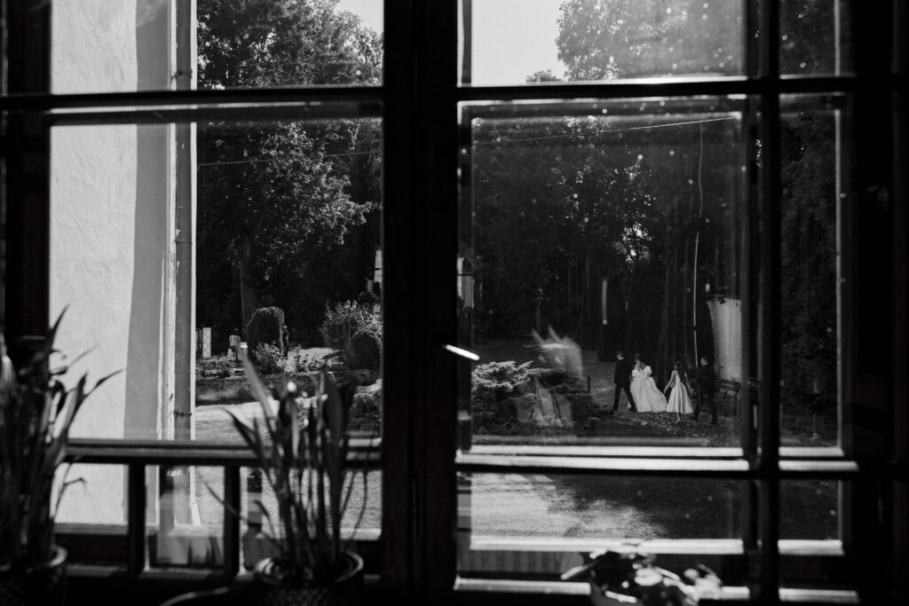 Widok na cudowną sesję ślubną przez okno, dzieci na spacerze w ogrodzie.