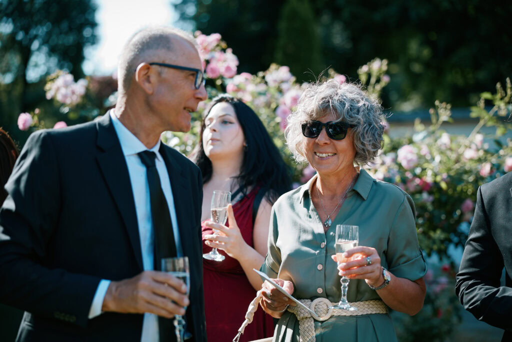 Eleganckie towarzystwo na przyjęciu na wolnym powietrzu, kwiatowe tło, świętowanie z drinkami.