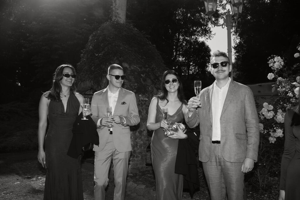 Grupa ludzi w eleganckim stroju, świętująca z kieliszkami szampana, w plenerze.