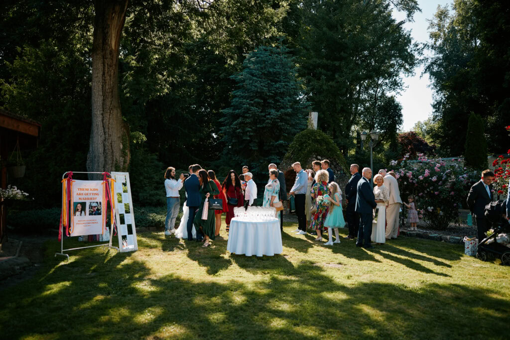Zdjęcie grupy gości podczas uroczystości ślubnej na zewnątrz w piękny, słoneczny dzień.