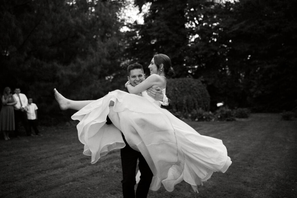 Alt text: Młoda para na weselu, pan młody tańczy z panną młodą w ogrodzie, uśmiech i radość.