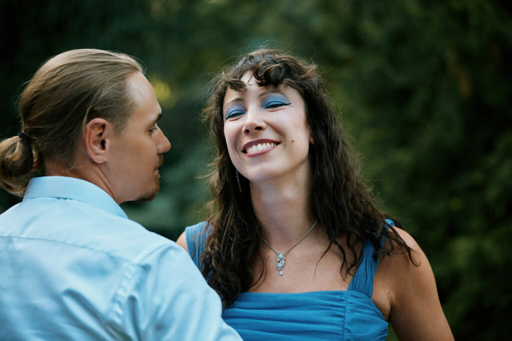 Alt: Uśmiechnięta kobieta w niebieskiej sukni i mężczyzna w jasnej koszuli podczas romantycznego spotkania.