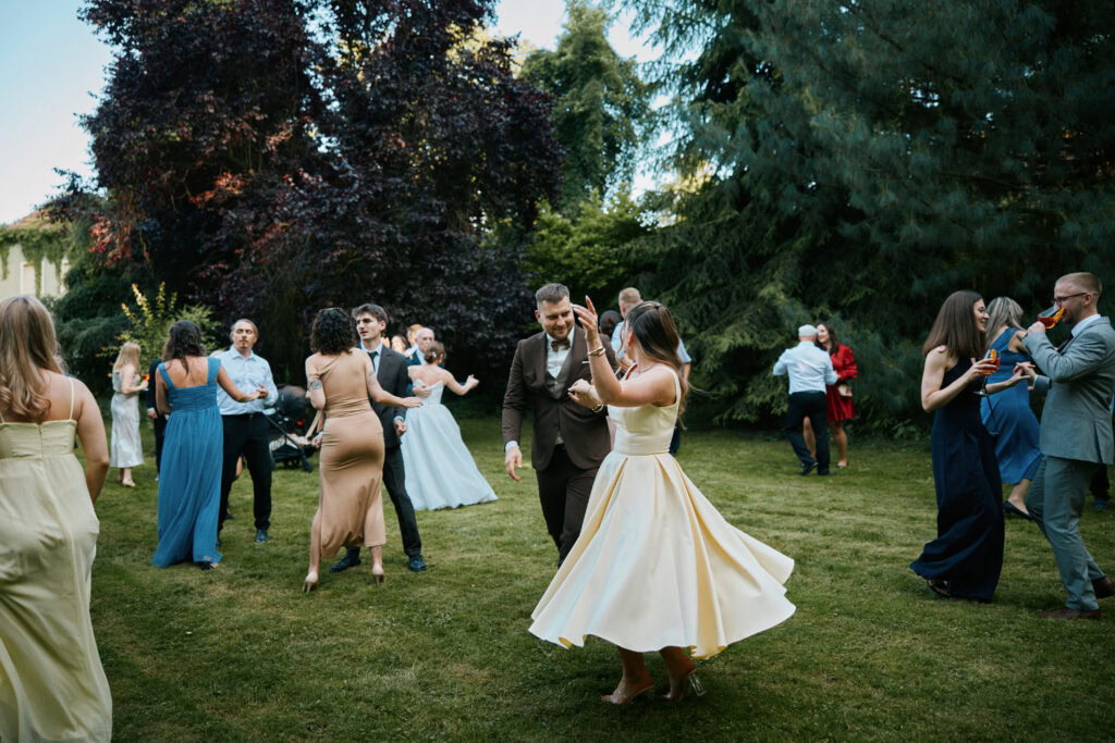Uczestnicy wesela tańczą na trawniku w ogrodzie.