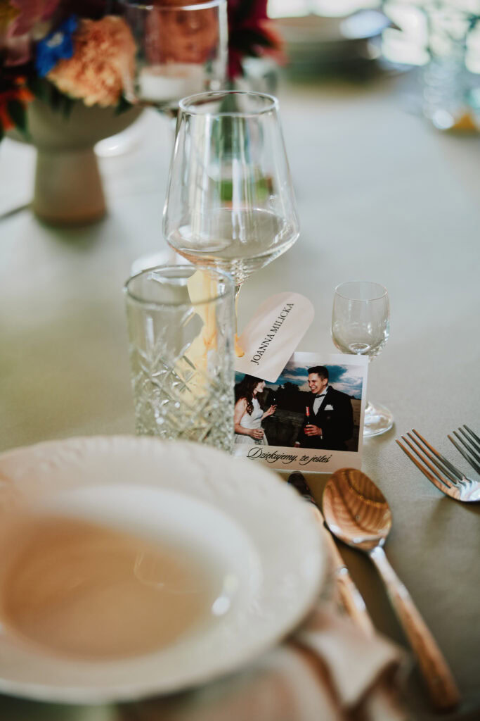 Alt: Dekoracja stołu weselnego z kieliszkami, świecami i zdjęciem nowożeńców.