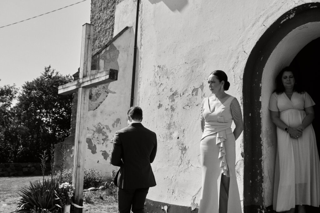 Alt tekst: Piękna ceremonia ślubna przed starą, malowniczą kaplicą z drzewami w tle.