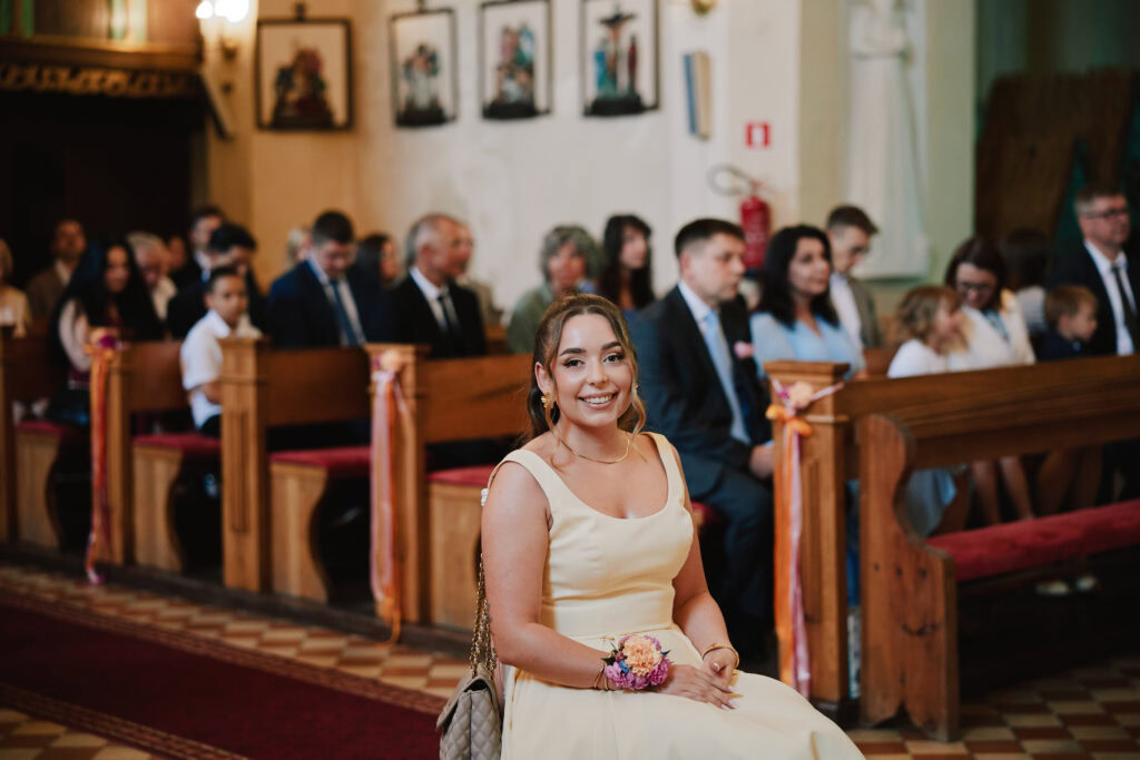 Sztuczny tekst alternatywny: Uroczystość ślubna w kościele, panna młoda siedzi uśmiechnięta.